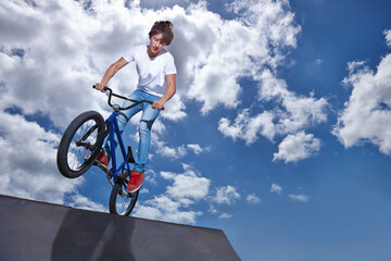 Riding, bike and teen on ramp for sport performance, jump or training for event at park with blue sky mockup. Bicycle, stunt or kid balance on edge of board in trick for cycling competition challenge
