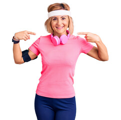 Obraz na płótnie Canvas Young blonde woman wearing sportswear and headphones looking confident with smile on face, pointing oneself with fingers proud and happy.