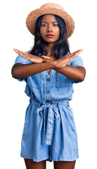 Young indian girl wearing summer hat rejection expression crossing arms doing negative sign, angry face