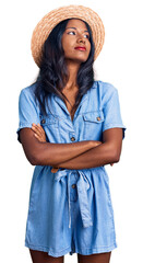 Young indian girl wearing summer hat looking to the side with arms crossed convinced and confident