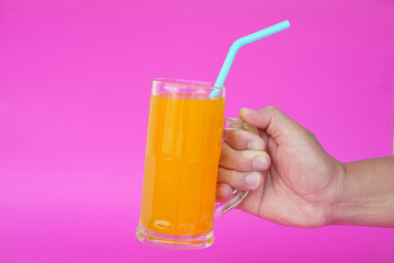 Close up of man hand holding glass of orange juice with drinking straw, on pink background. Concept, morning refreshing beverage. Sweet, testy and high vitamin C.          - obrazy, fototapety, plakaty