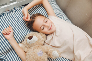 Top view of cute little girl stretching in bed, yawning and rubbing her eyes, waking up early in...