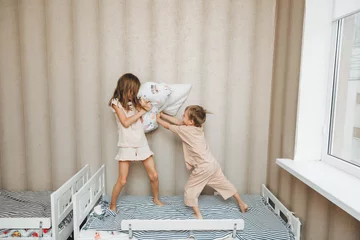 Foto op Plexiglas Naughty children A little boy and a girl had a pillow fight on the bed in the bedroom. brother and sister playing with pillows on the bed © inna717