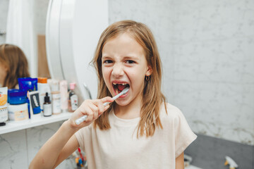 Happy little girl brushing her teeth in front of a bathroom mirror. Morning hygiene.