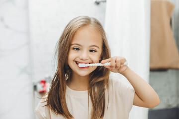Portrait of a girl with Down syndrome brushing her teeth. Happy little girl brushing her teeth in...