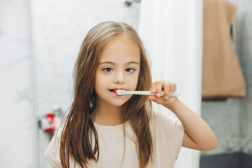 Portrait of a girl with Down syndrome brushing her teeth. Happy little girl brushing her teeth in...