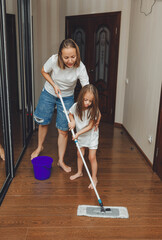 a little daughter and her mom clean the house, a child washes the kitchen floor, a cute little helper girl cleans the floor with a mop, a happy family cleans the room.