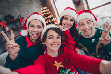 Photo of group funky excited buddies toothy smile make selfie demonstrate v-sign decorated apartment indoors
