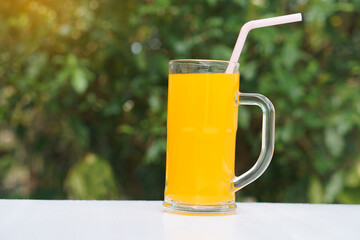Glass mug of orange juice with drinking straw. Outdoor background. Concept, morning refreshing beverage. Sweet, testy and high vitamin C.