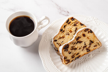 Stollen and hot coffee on a table. Cup of hot coffe and two slices of traditional German Holiday bread of nuts, spices, and dried fruits on a white plate. Close-up of Cristmass sweet breakfact.