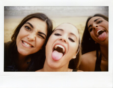 Instant Shot Of Three Funny Girls Sticking Out Tongues. Three young friend making selfie while sticking out tongues and smiling at camera