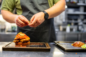 chef hand cooking cheeseburger with vegetables and meat on restaurant kitchen
