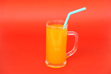 Glass mug of orange juice with drinking straw. Red  background. Concept, morning refreshing beverage. Sweet, testy and high vitamin C.          - obrazy, fototapety, plakaty