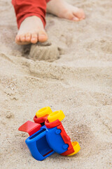Fototapeta na wymiar Little car, children toys and feet of little boy. Relax or playing on sand at beach. Summer and vacation time