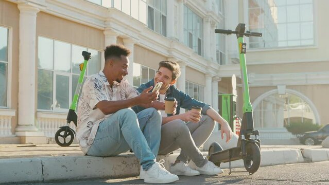 Two friends having fun drinking coffee with shared electric push scooters in the city.