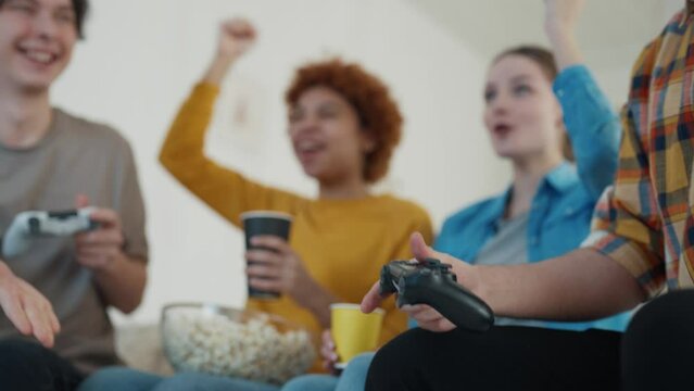 Two guys competing playing video games and girls cheering them. One guy wins and happy about victory, other gets upset. Diversity company of people friends hanging together. Leisure, entertainment.