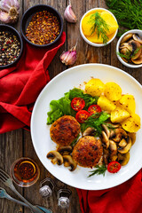 Fried pork meatballs with boiled potatoes and fried mushrooms on wooden table
