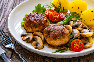 Fried pork meatballs with boiled potatoes and fried mushrooms on wooden table
