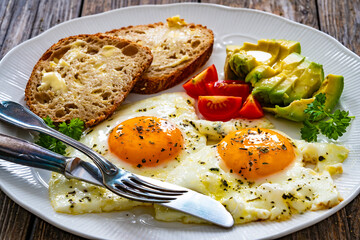 Breakfast - sunny side up egg, toasted bread and avocado served on wooden table
