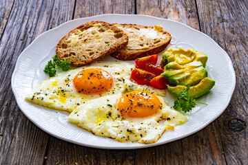 Breakfast - sunny side up egg, toasted bread and avocado served on wooden table
