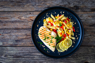 Grilled chicken breast with penne noodles, lemon and pepper on wooden background
