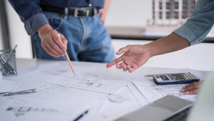 Two engineer architect pointing on blueprint of sketching interior architectural building to discussion technical for construction plan and building model while working together in workplace site