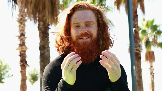 handsome redhaireb man with long beard wear black sporty suit talking with somebody in sunny beach