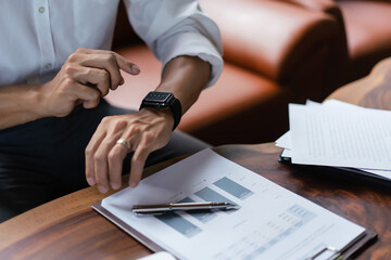 Hands of businessman checking time on smartwatch while working about financial document of business - obrazy, fototapety, plakaty