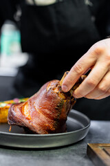 chef hand cooking Baked Pork knuckle with vegetables on plate in kitchen