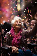 Elderly grandmother sits on wheelchair and enjoys flying confetti, happiness, joy, street festival, holiday, carnival