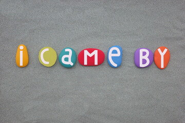 I came by, creative slogan composed with hand painted multi colored stone letters over green sand
