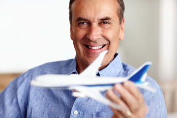 Mature man, portrait and toy plane for travel, vacation and holiday planning with a smile at home. Happy, airplane model and retirement of a male person with confidence from trip and air traveling