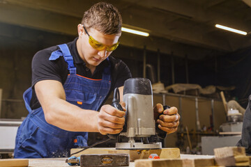 A young  man wearing safety goggles carpenter builder pre-works the edges of the wooden board with...