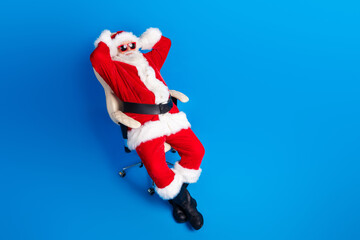 Full size photo of pensioner senior man sit relaxed arms behind head wear trendy santa claus costume coat isolated on blue color background