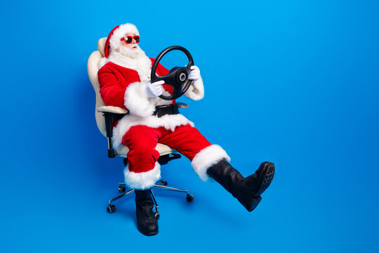 Full length photo of mature pensioner man sit armchair hold rudder wear trendy santa claus costume coat isolated on blue color background