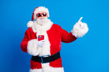 Photo portrait of elderly retired man hold gadget point empty space wear trendy santa claus costume coat isolated on blue color background