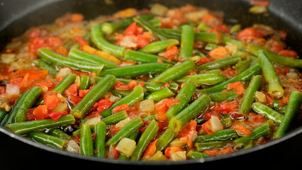 Frying in pan vegetables green beans, tomatoes, bell peppers