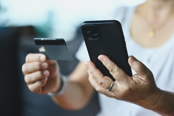 Close-up mature woman using a phone, holding a credit or debit card, making internet payments, shopping or browsing online banking services, entering information