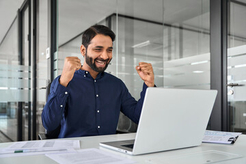 Happy Indian business man employee manager winning prize online working using laptop in office....