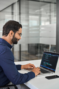 Busy Indian business man software developer engineer working on laptop computer in office. Male administrator programmer specialist coding on pc developing applications programming code. Vertical.