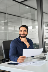 Happy Indian professional business man company manager sitting at desk in office looking at camera...