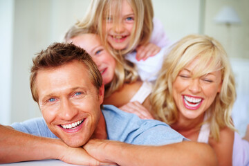 Portrait, love and a family laughing on a bed together while in the home on a weekend morning. Face, smile and a funny father, mother and children in the bedroom of an apartment to relax for bonding