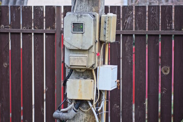 a lot of gray plastic electric and gas meters hang on a concrete post near a brown wooden fence...