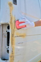 Preparing the car for painting, rubbing the surface to remove old paint and applied putty, after treating with primer. Paint and varnish work in a car repair shop