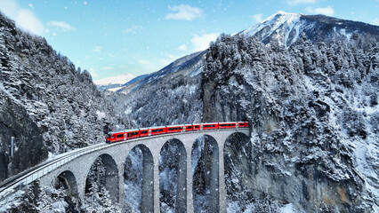 Snow falling and Train passing through famous mountain in Filisur, Switzerland. Train express in Swiss Alps snow winter scenery. - obrazy, fototapety, plakaty