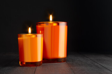 New Year orange burning candles in orange glass in darkness on black wood table, copy space. Festive background for advertising, design, text, poster, flyer.