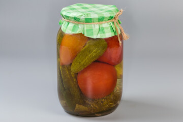 Canned cucumbers with tomatoes in jar on a gray background