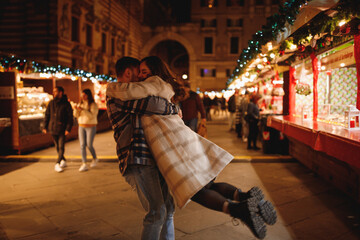 Young stylish couple in love in checkered coats dancing at Christmas market in Verona 