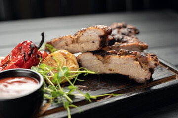 Hot grilled spare ribs from a summer BBQ served with a chili pepper and tomatoes sauce on an wooden cutting board
