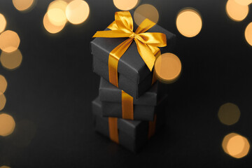 Black gift box with golden ribbon bow on black background